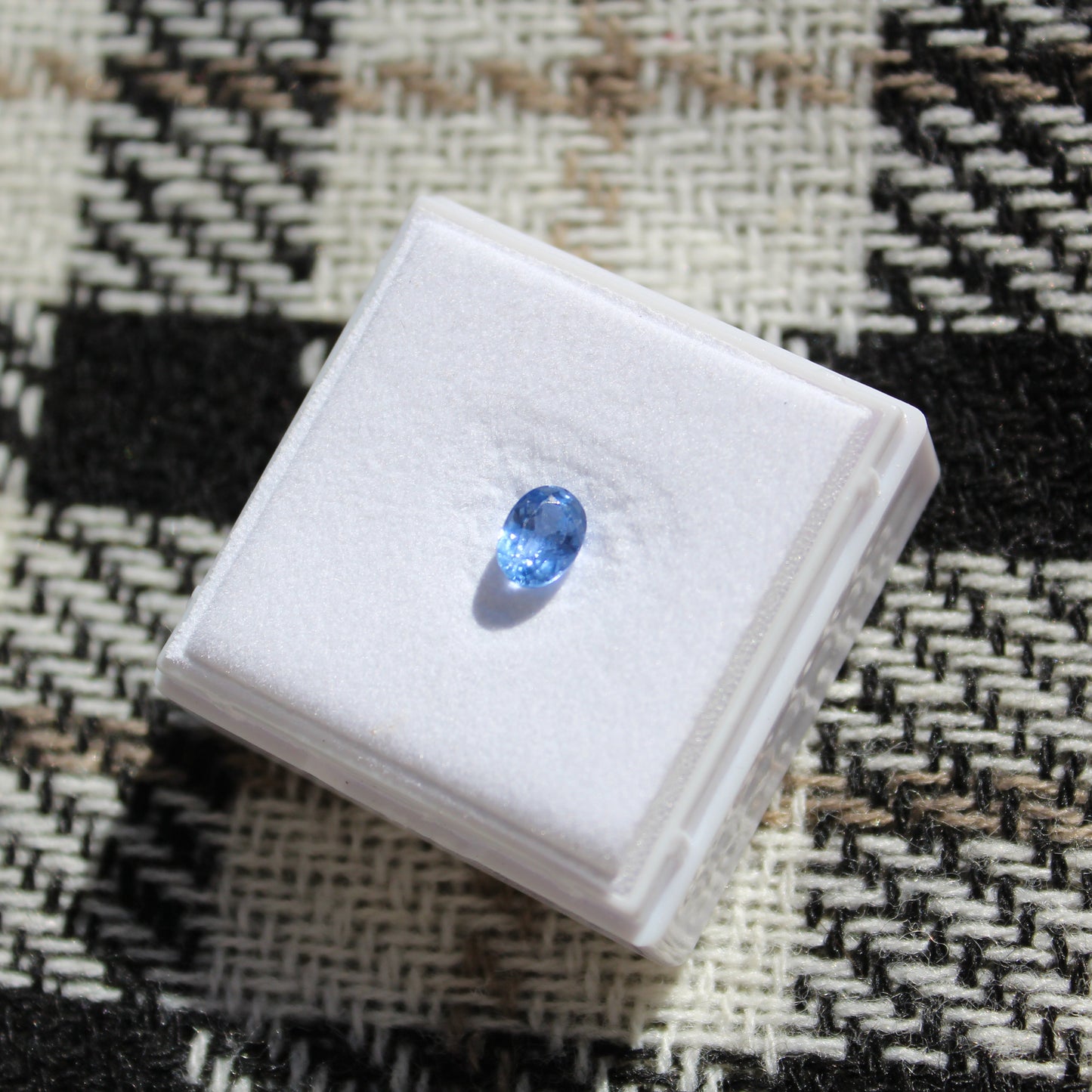 Blue gemstone on a white box against a patterned fabric background