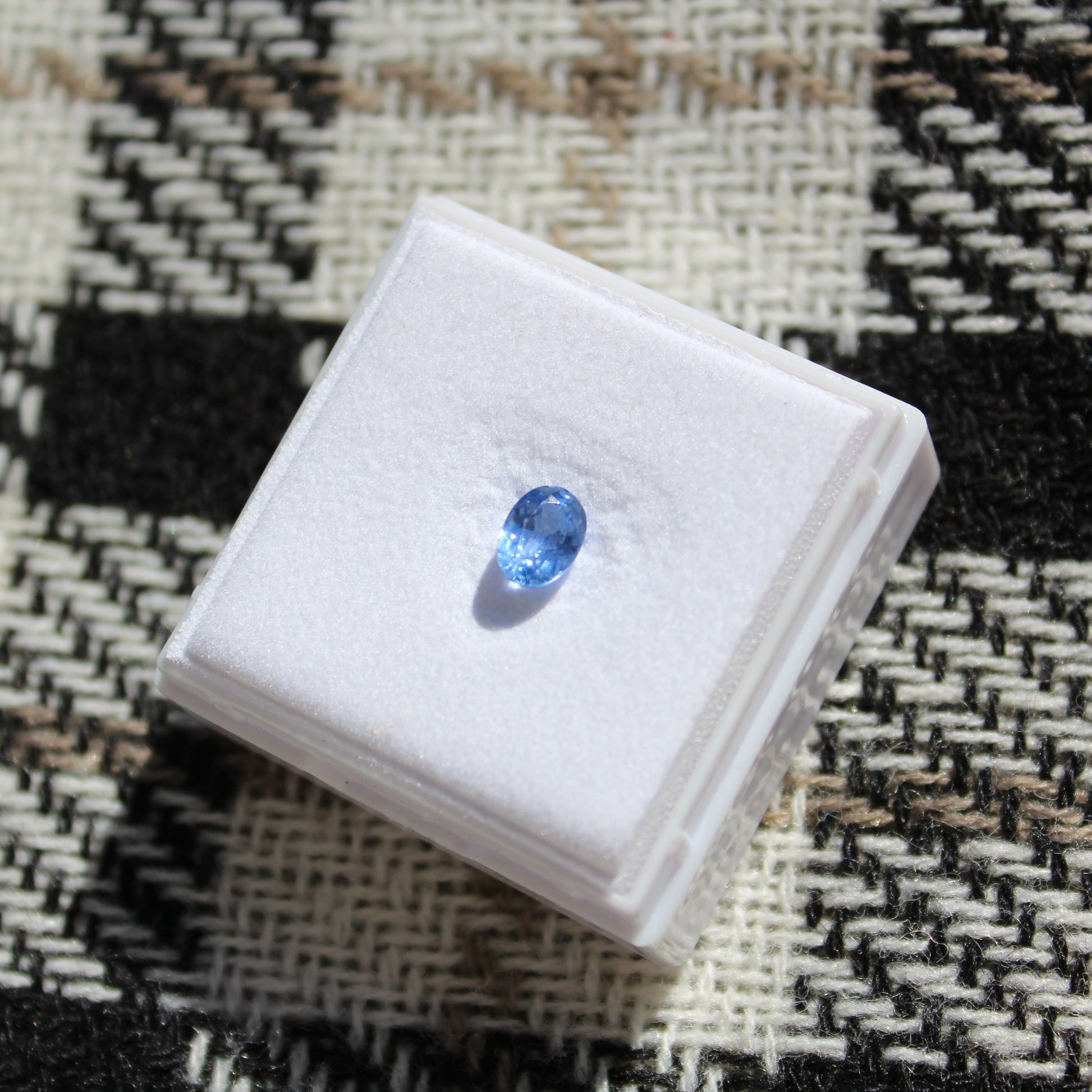 Blue gemstone on a white box against a patterned fabric background