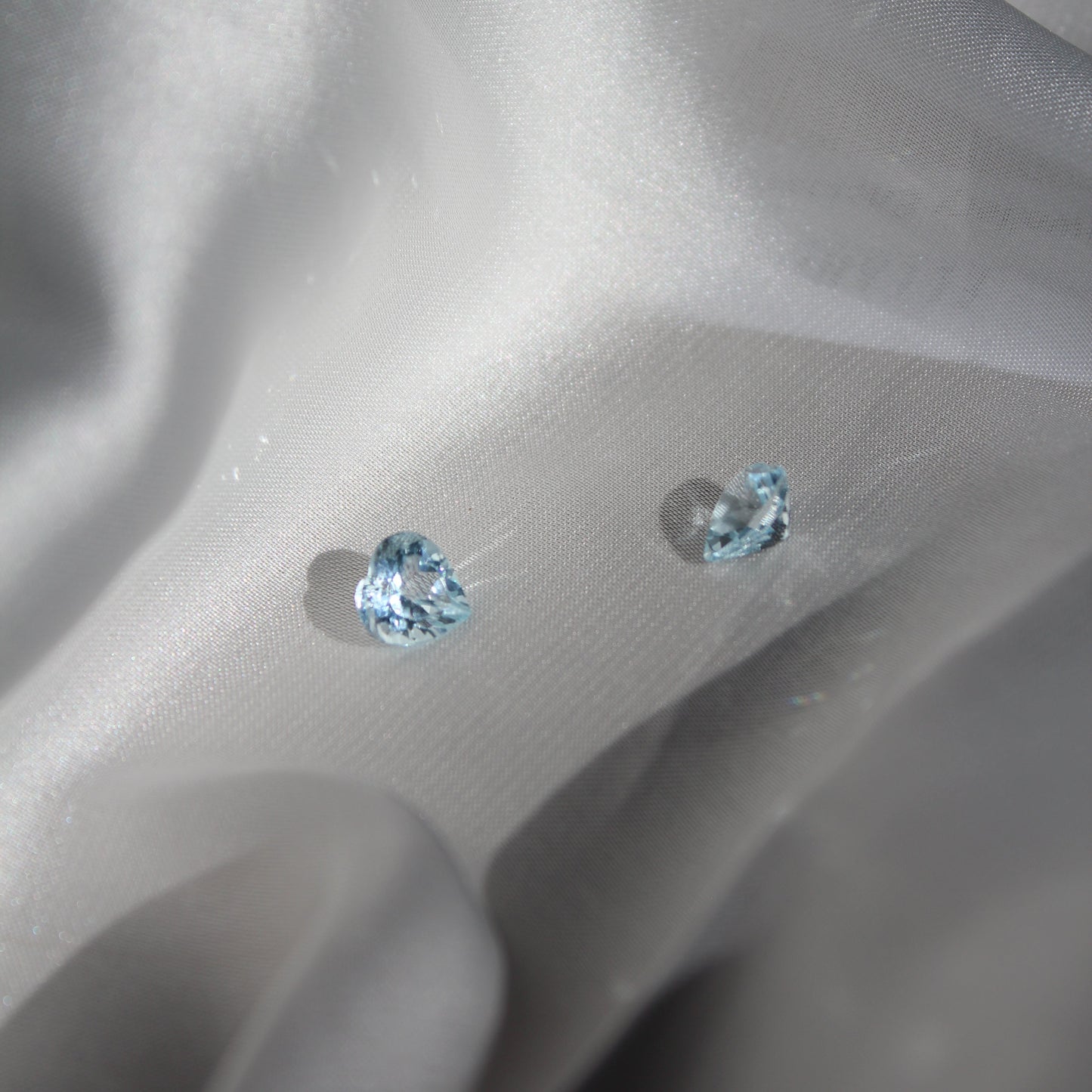 Two heart-shaped blue gemstones on a white silk surface