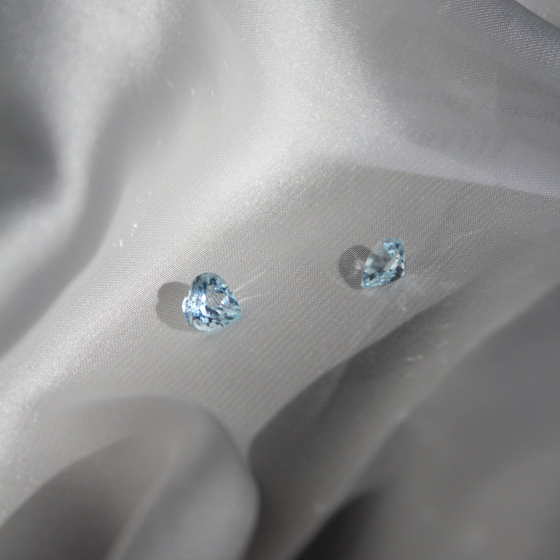 Two heart-shaped blue gemstones on a white silk surface