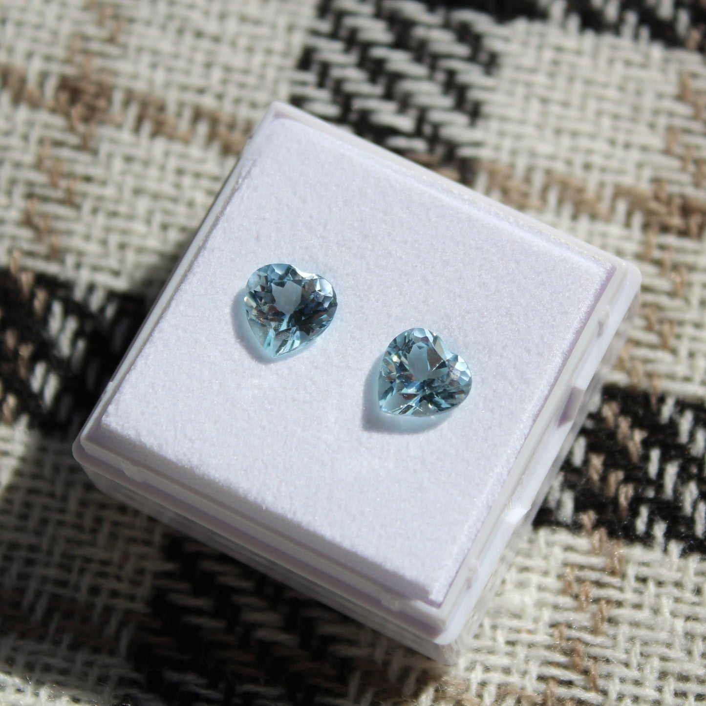 Pair of blue gemstone earrings on a white display box with a patterned fabric background