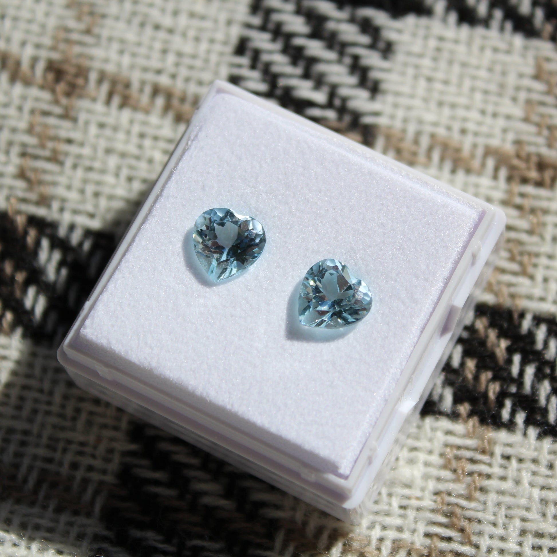 Pair of blue gemstone earrings on a white display box with a patterned fabric background