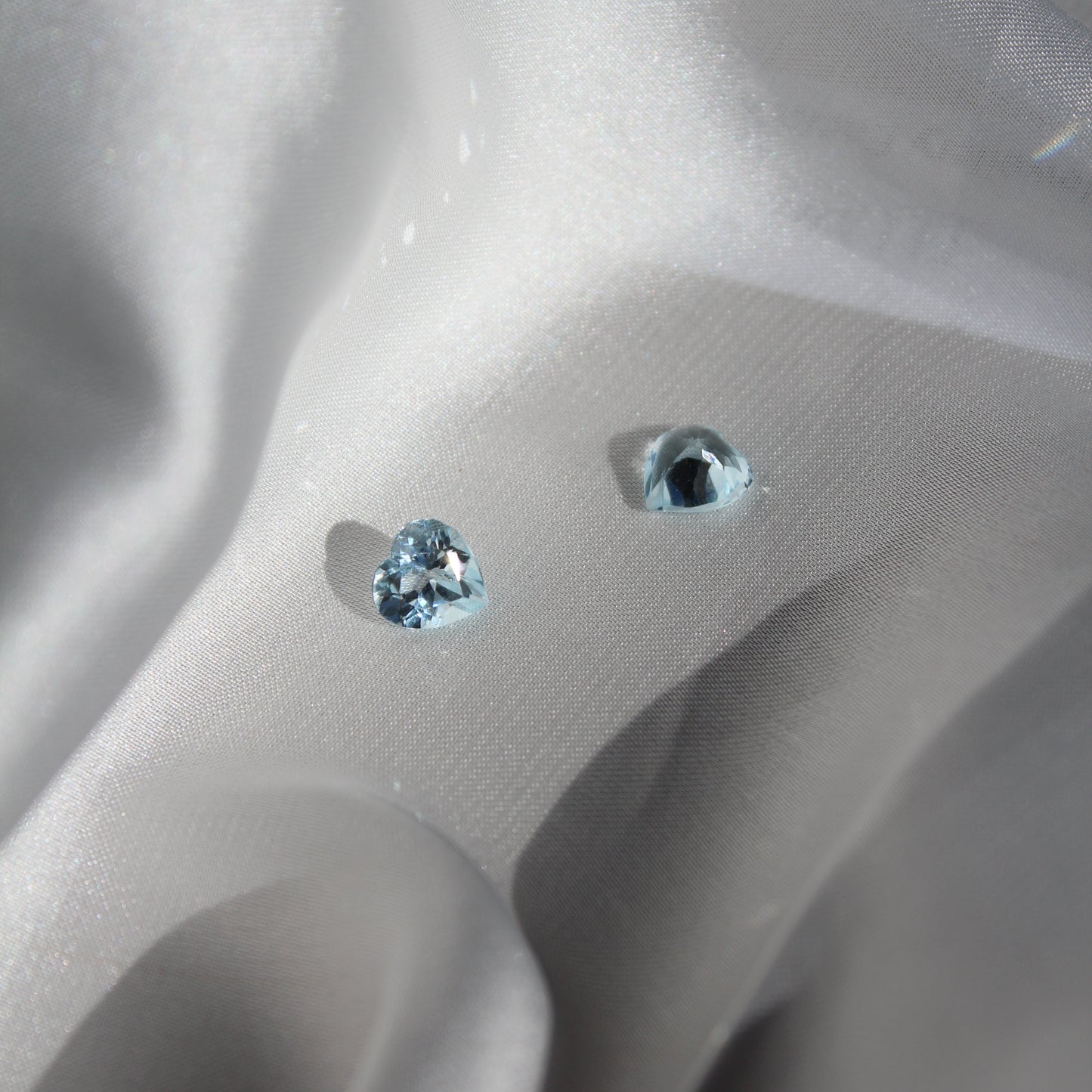 Two heart-shaped blue gemstones on a white silk surface
