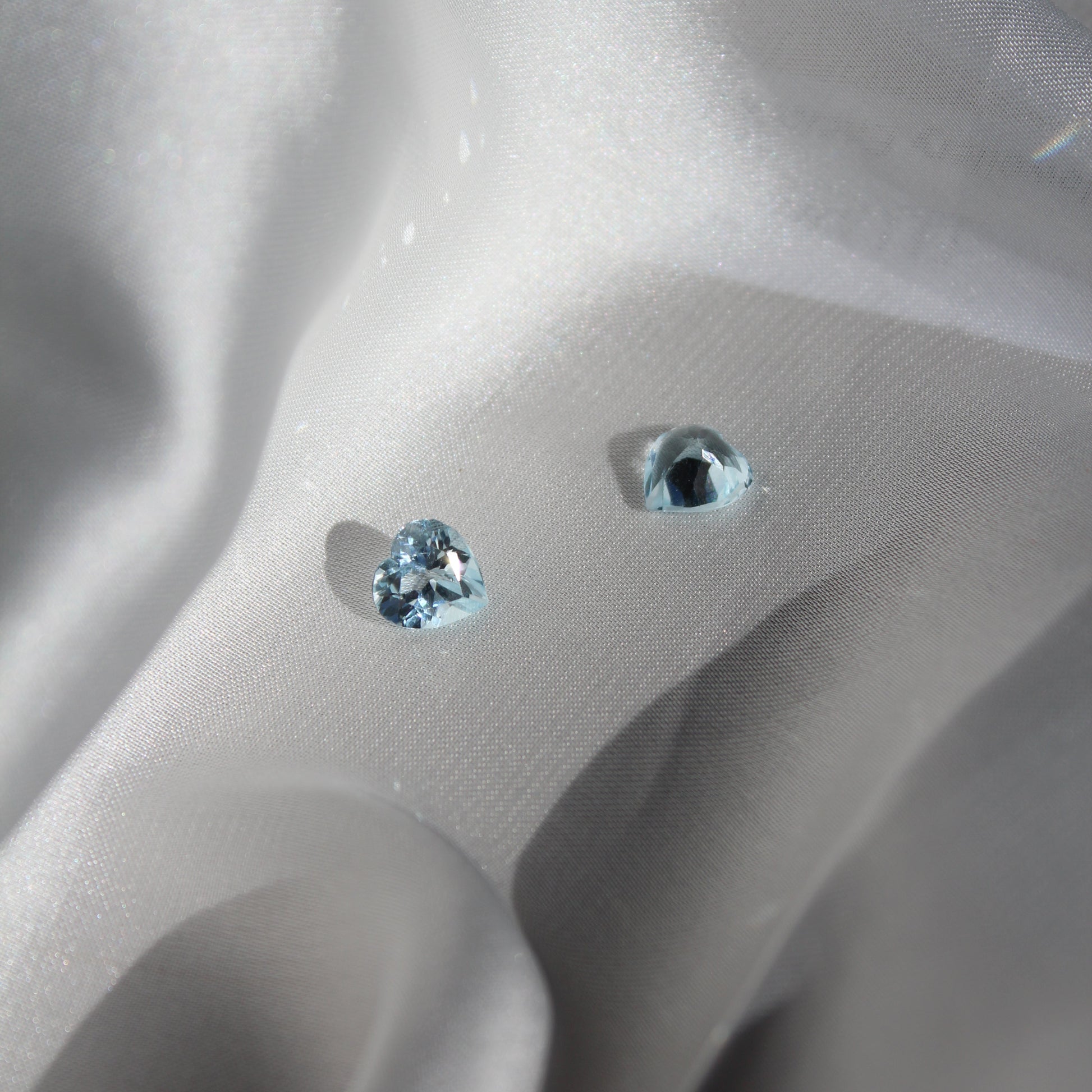 Two heart-shaped blue gemstones on a white silk surface