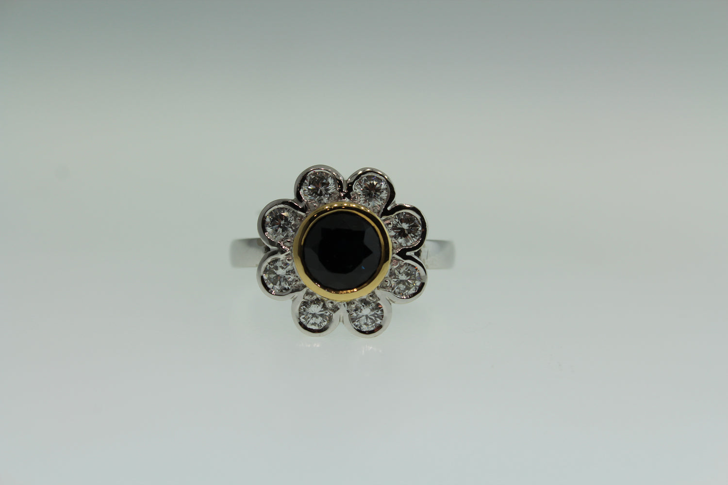 Ring with black gemstone center surrounded by diamonds on a white background