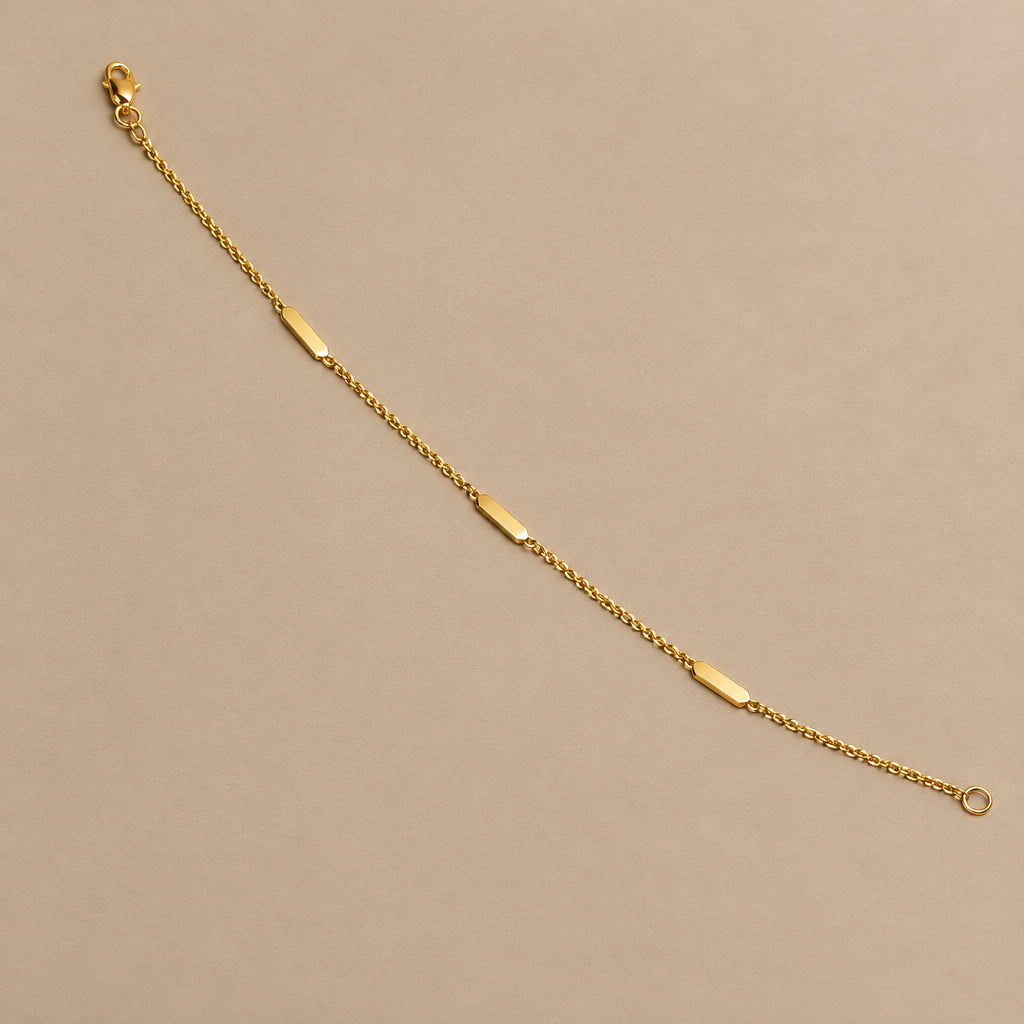 A delicate gold chain bracelet with three small polished oval metal accents