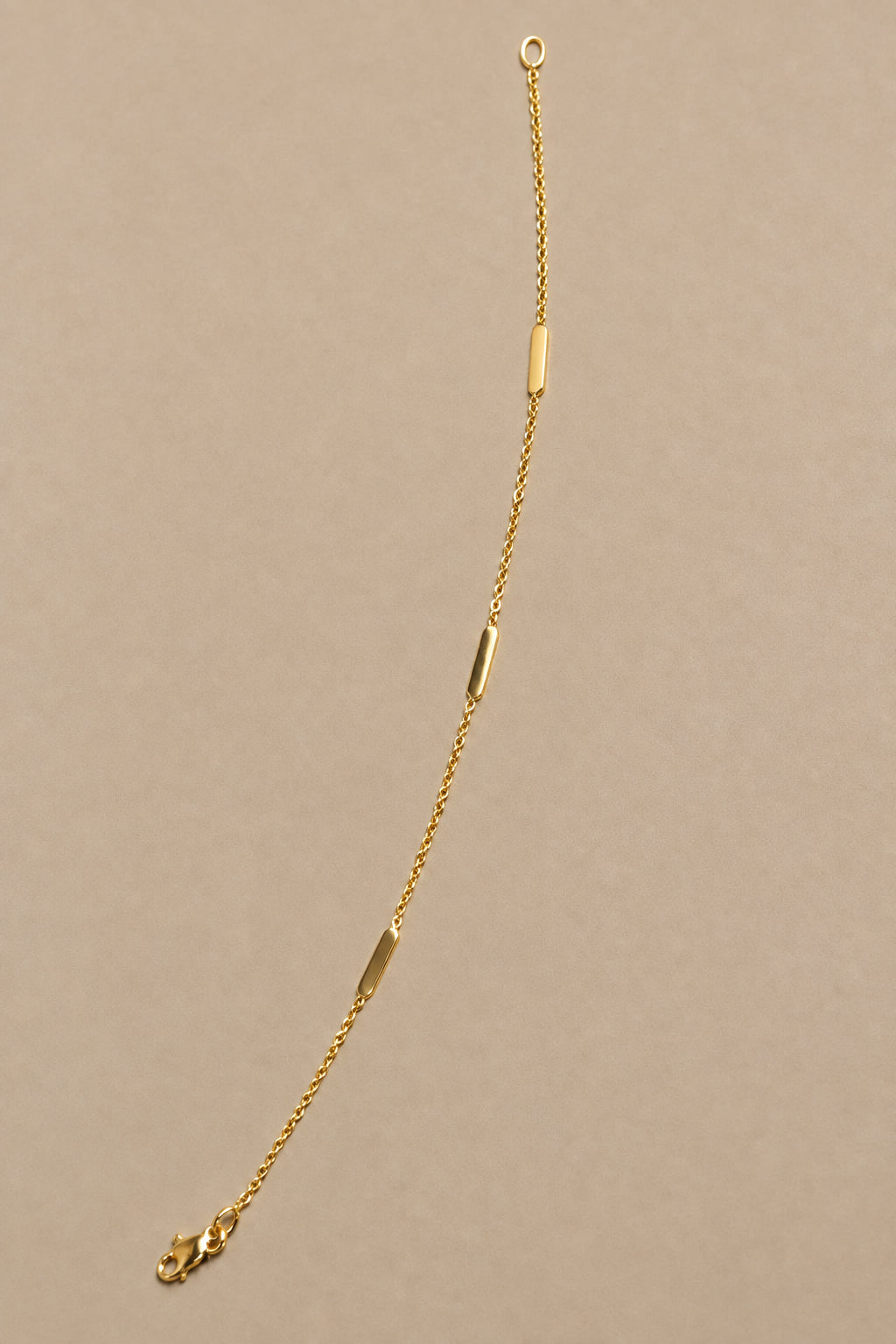 A delicate gold chain bracelet with three small polished oval metal accents
