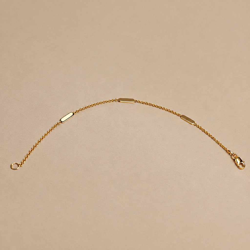 A delicate gold chain bracelet with three small polished oval metal accents