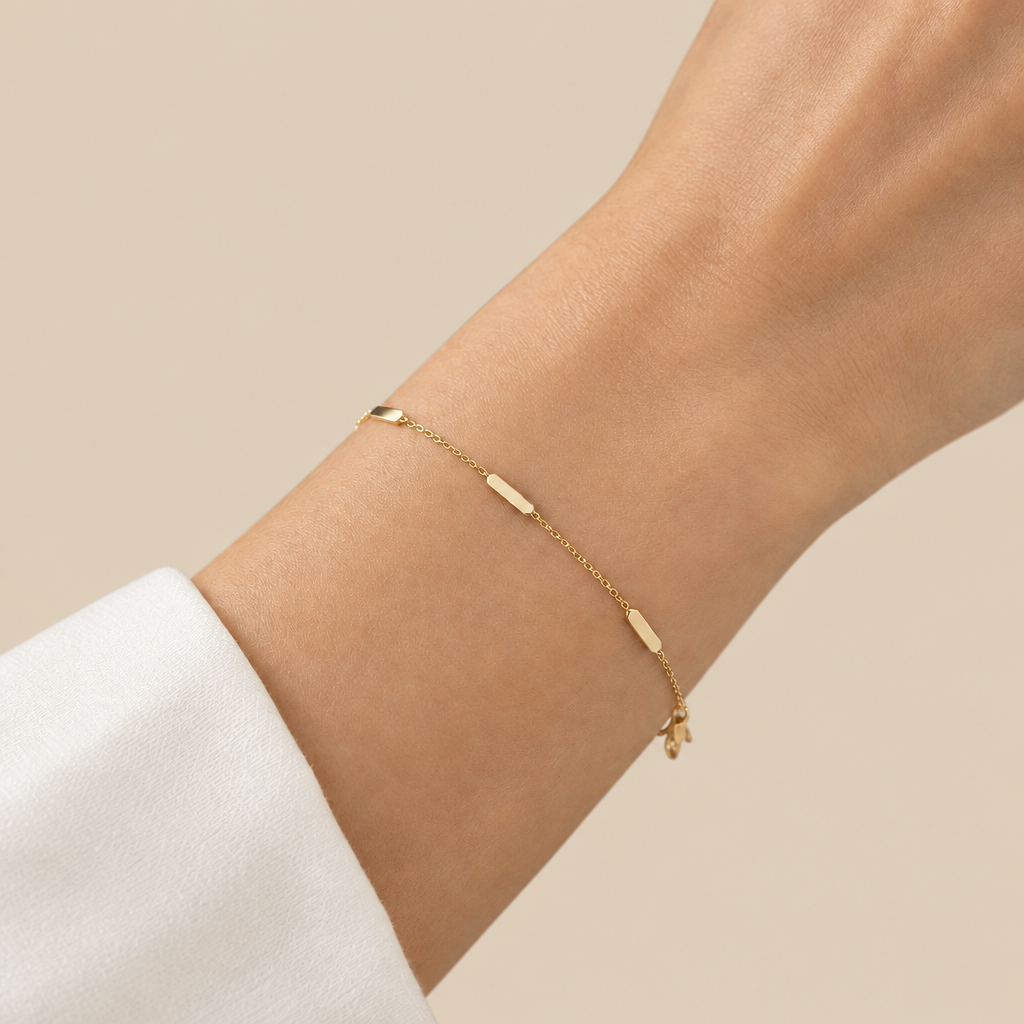 A delicate gold chain bracelet with three small polished oval metal accents, modeled on a womans wrist