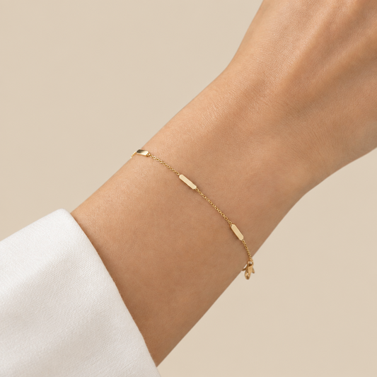 A delicate gold chain bracelet with three small polished oval metal accents, modeled on a womans wrist