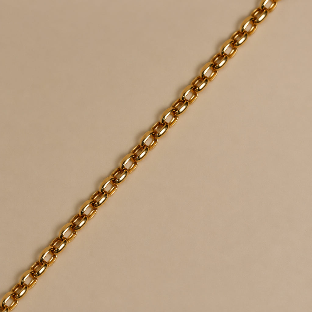 A close up of a gold belcher chain bracelet, displayed on a plain beige background.
